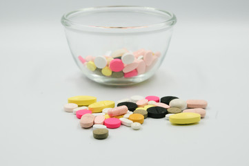 Assorted pharmaceutical medicine pills, tablets and capsules with thermometer on glass bowl