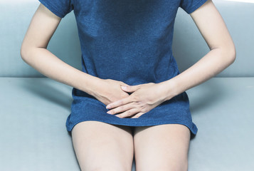 Beautiful Attractive Asian woman wearing white shirt sitting on bed have a bladder pain or uti pain...