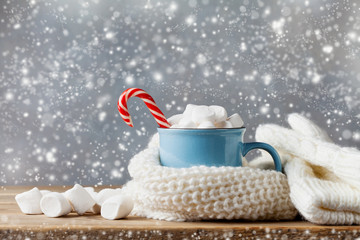 Winter lifestyle with cup of hot cocoa with marshmallows and knitted scarf on wooden background....
