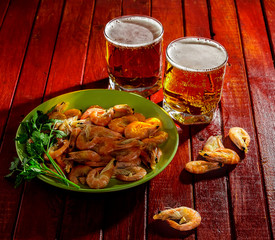 Two Beers and a plate of prawns and parsley on the table.