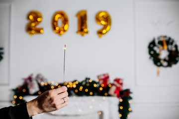 Sparkling Bengal fire in man hand on white background with yellow ballons numbers 2019. Christmas Holiday Concept