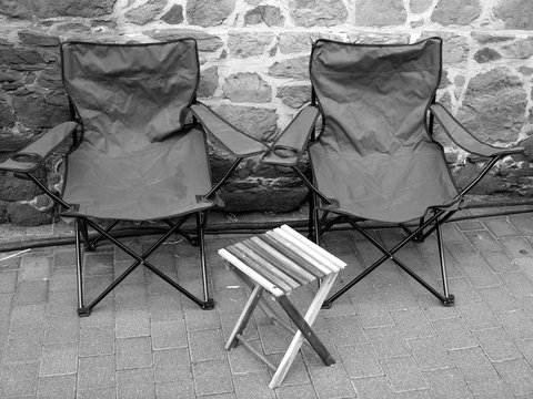 Verlassene klappbare Regiest&uuml;hle mit Holztisch vor einer Mauer aus Naturstein auf dem B&uuml;rgersteig beim Oldtimertreffen Golden Oldies in Wettenberg Krofdorf-Gleiberg bei Gie&szlig;en in Hessen in Schwarzwei&szlig;