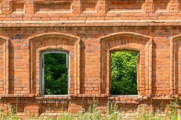 Two windows of the old destroyed building of red brick through which you can see green plants.