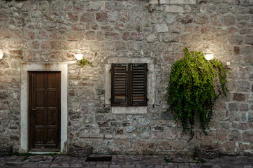 Facade of old house with a wooden door and a window, lit by two lanterns.