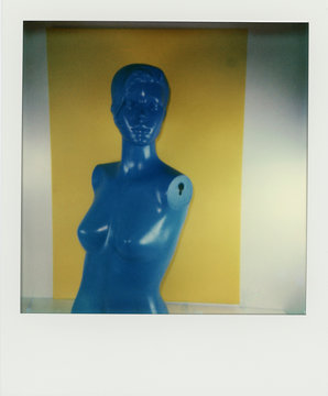Polaroid scan of a blue mannikin torso in front of yellow and white background