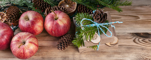 Web banner Christmas background. Red apples, gifts, fir branches and cones on a wooden background