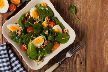 Delicious salad of fresh spinach, boiled egg, tomatoes, nuts and sunflower seeds