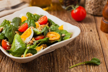 Delicious salad of fresh spinach, boiled egg, tomatoes, nuts and sunflower seeds