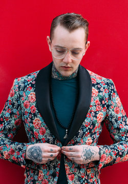 Tattooed handsome man with colourful flower jacket over red background