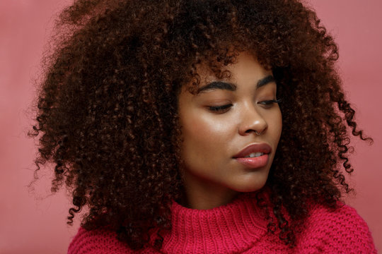 Portrait of a young African American afro woman in pink studio smiling looking away