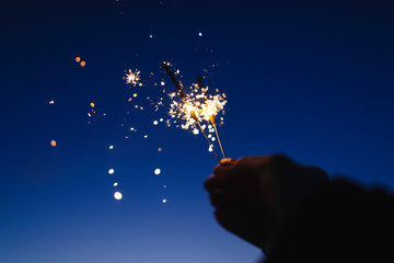 Female hand holding sparkler against a dark sky