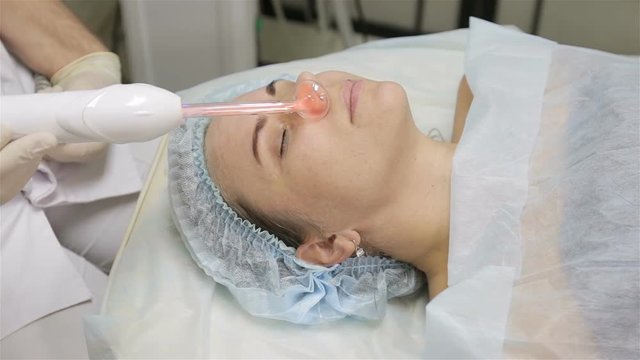 Woman getting facial electric darsonval therapy at cosmetology clinic