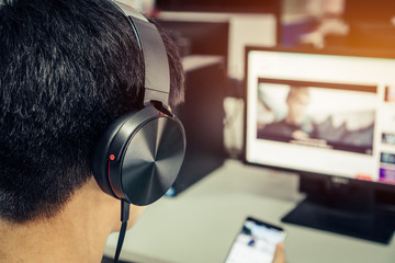 Student learning online study concept: Asian Younf man listening with Headphones and laptop, sitting holding smartphone chatting in home for e-learning in educational technology by self