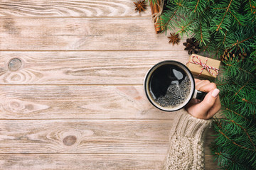 Woman holding cup of hot coffee on rustic vintage wooden table. hands in warm sweater with mug, winter morning or christmas concept, top view