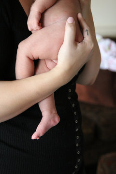 Mother holds newborn, tattoo of cross on her finger