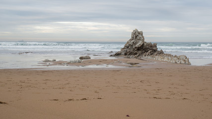 Fototapeta na wymiar Pequeña cresta de roca piramidal emergiendo del mar cantabrico en la playa de Arrietara en Sopela, Bizkaia