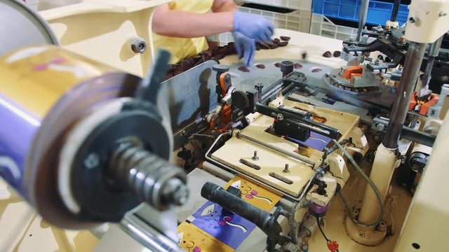 Modern industrial machine wrapping tasty sweets and putting them on conveyor on confectionery factory.