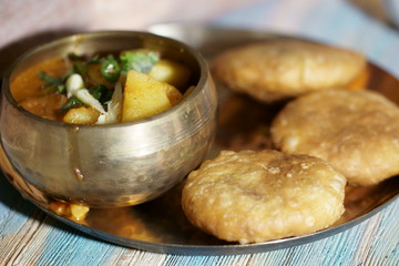 A plate of Khasta Kachauri with a bowl of spicy and tangy Potato sabji or curry.