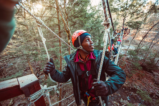 A young man leads a group of friends through a rope bridge during an outdoor zip line course