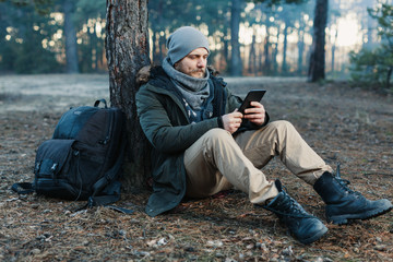 adult handsome Male traveler Sits On autumn pine forest Near tree, Holding At Tablet Recreation Resting Travel Destination Concept