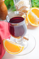 Mulled wine with cinnamon sticks in glass and cookies on wooden table with christmas tree branch on background