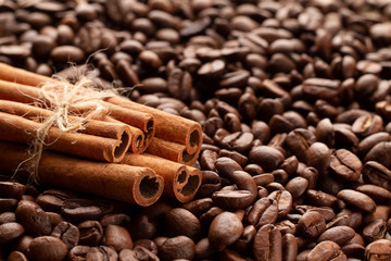 Obraz na płótnie Canvas Bunch of sticks of fragrant cinnamon lies on freshly roasted coffee beans in the lower left third of the frame in a golden section. Photo of coffee beans and cinnamon in backlight.