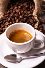 in the foreground, espresso cup. In the background heap of roasted coffee beans