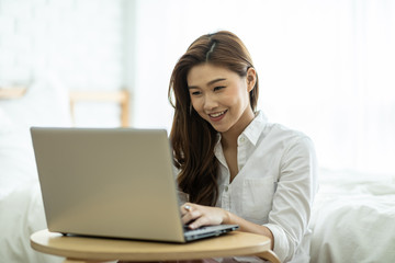 Lifestyle of Beautiful Attractive Asian woman smile working or shopping online with computer laptop in bedroom feeling so happiness and cheerful,Relax in holiday with laptop and using social network