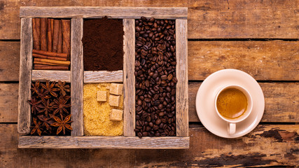 on the rustic wooden table, with a top view, a cup of espresso, a wooden container with various spices, raw sugar and coffee beans