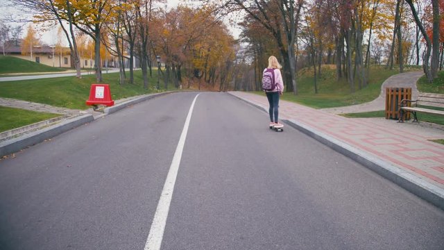 Young pretty beautiful blond hipster woman in pink windstopper having fun riding skateboard longboard downhill on beautiful road in slow motion