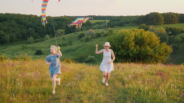 A young mother with a girl with two pigtails resting in nature, playing with an air kite.