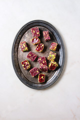 Variety of traditional turkish dessert Turkish Delight different taste and colors with rose petals and pistachio nuts on vintage tray over white marble background. Flat lay, space