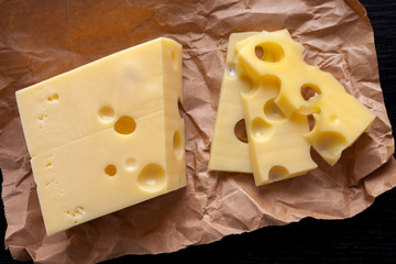 sliced emental cheese on kraft paper and dark wooden background