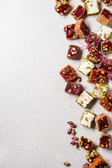 Variety of traditional turkish dessert Turkish Delight different taste and colors with rose petals and pistachio nuts over grey spotted background. Flat lay, copy copy space