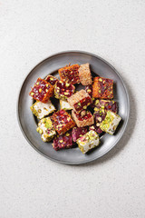 Variety of traditional turkish dessert Turkish Delight different taste and colors with rose petals and pistachio nuts on vintage metal plate over grey spotted background. Flat lay, copy space