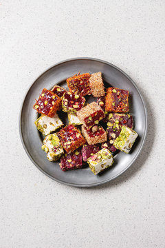 Variety of traditional turkish dessert Turkish Delight different taste and colors with rose petals and pistachio nuts on vintage metal plate over grey spotted background. Flat lay, copy space