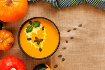 Pumpkin soup puree with cream and pumpkin seeds on the background of whole pumpkins of different colors. The surface of the textile