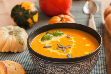 Pumpkin soup puree with cream and pumpkin seeds on the background of whole pumpkins of different colors. The surface of the textile
