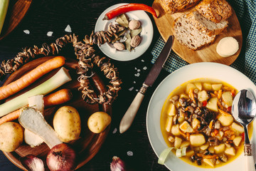 Homemade mushroom soup of dried porcini mushrooms with potatoes, bread and other vegetables on a dark wood table. Vegetables and spices