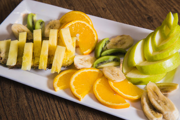 sliced fruits in a white plate are on the table - proper nutrition, raw foods, vegetarianism, pineapple, apple, orange, banana and kiwi