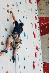 Sportive man climbs up on artificial rock wall