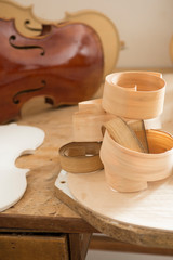 Wood shaving curls on table, and Cello or, violoncello, in background of craftsman's workshop