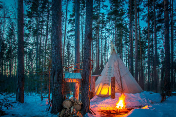 TIPI. Winter. Tipi stands in the winter forest. Bonfire in the forest. Eco-friendly tourism. National dwellings. National Indian dwellings. © Grispb