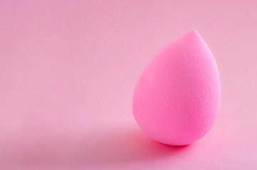 Face foundation application tool and makeup products concept with a beauty blender sponge isolated on a pink background and copy space