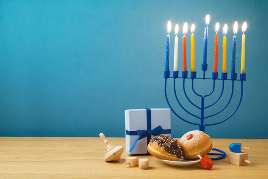 Jewish holiday Hanukkah background with menorah, sufganiyot, gift box and spinning top on wooden table