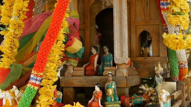 Wooden miniature guardian spirit house. Small buddhist temple shrine, colorful flower garlands. San phra phum erected to bring fortune. Traditional respect animistic rituals, pray ceremonies