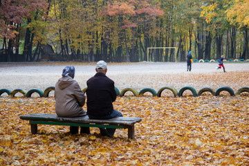 Couple of elderly people sit on a bench in the autumn Park. People.