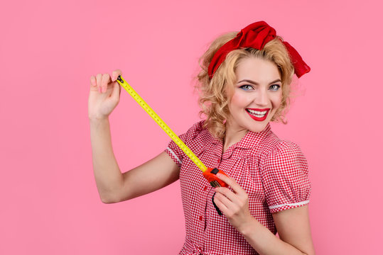 Woman in pin-up style holds ruler. Pin-up girl holds construction ruler. Woman in red dress holds construction roulette. Sale. Discount. Engineering. Tape measure construction tool. Measurement tape.