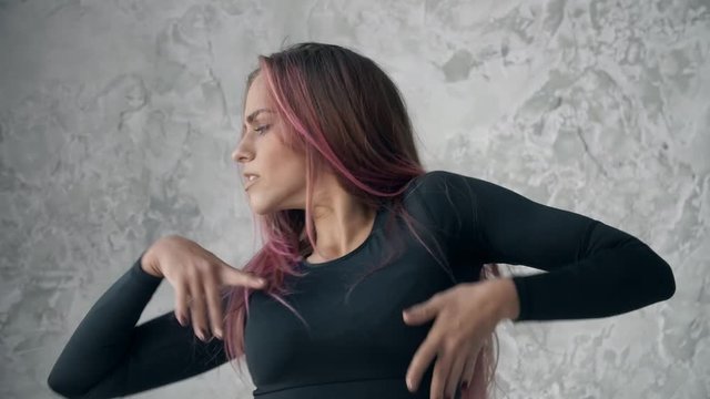Beautiful young woman with pink hair, dancing professionally seductive dance on gray background
