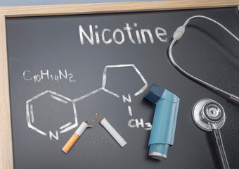 Formula chemical nicotine written and drawn with chalk on a blackboard, next to an inhaler and a stethoscope, conceptual image